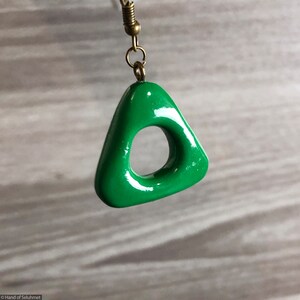 以下が含まれることがあります： 中央に穴が開いた緑色の三角形のイヤリング。イヤリングはポリマークレイ製で、光沢のある仕上げです。