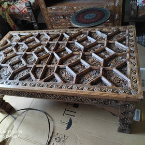 May include: A wooden coffee table with intricate carvings in a geometric pattern. The table has a dark brown finish and four legs.