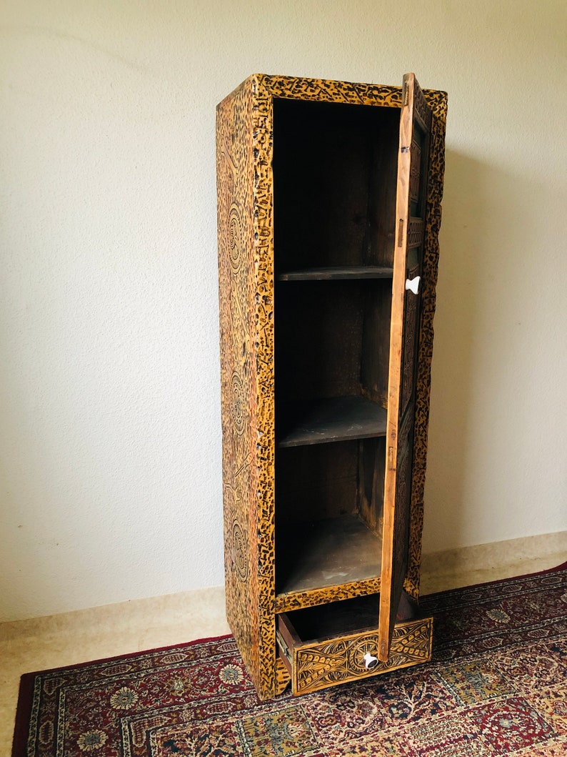K&ouml;nnte beinhalten: Ein hoher Holzschrank mit einer einzigen T&uuml;r und einer Schublade. Der Schrank ist mit aufwendigen Schnitzereien verziert und hat eine dunkelbraune Oberfl&auml;che.