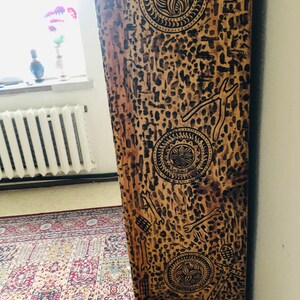 K&ouml;nnte beinhalten: Ein Holzbrett mit brauner Beize und schwarzen Markierungen. Die Markierungen sind kreisf&ouml;rmig und &auml;hneln einer stilisierten Blume. Das Brett ist eine vertikale Fl&auml;che und hat eine raue Textur.