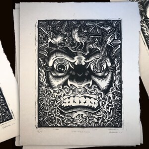 May include: Black and white woodblock print of a face with a snarling expression. The face is surrounded by vines and leaves. The print is titled "The Wild Man".