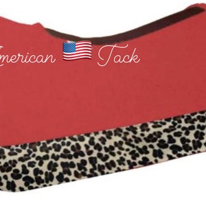 Peut inclure: Un tapis de selle rouge avec une bordure imprimée léopard. Le texte "American Tack" est présent avec un drapeau américain. Cet article équestre est conçu pour le confort et le style.