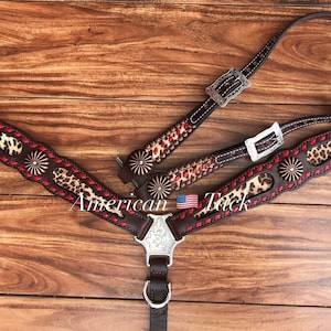 May include: Brown leather horse breast collar with red stitching and a leopard print design. The collar has silver buckles and conchos. The text "American Tack" is visible in the image.