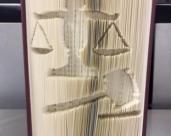 May include: A book with pages folded into a three-dimensional design of a sailboat. The book is bound in a dark red cover.