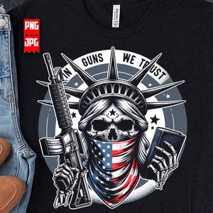 May include: Black t-shirt featuring a graphic of the Statue of Liberty as a skull, holding a rifle and a book, with an American flag bandana. The text reads "IN GUNS WE TRUST" in a circular design.