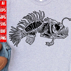 May include: A gray t-shirt with a black and white illustration of a anglerfish skeleton. The fish has a large mouth with sharp teeth and a long, thin lure.