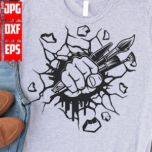 May include: A black and white graphic design of a fist breaking through a wall, holding paintbrushes. The design is on a grey t-shirt.