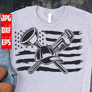 May include: A gray t-shirt with a black and white design of a wrench, a plunger, and a baseball cap crossed over a distressed American flag.