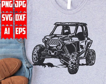 Pode incluir: Uma camiseta cinza com uma silhueta preta de um veículo off-road. O veículo tem uma gaiola de proteção e quatro rodas. A camiseta está sobre uma superfície de madeira.