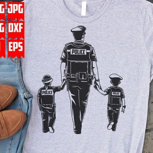 以下が含まれることがあります： 警察官が2人の子供と歩いている黒と白のイラストが描かれた灰色のTシャツ。警官と子供たちは全員、警察の帽子をかぶり、「POLICE」と書かれたバッジをつけています。
