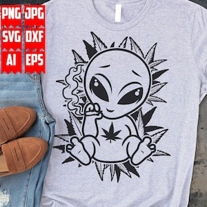 May include: Black and white graphic design of an alien smoking a joint surrounded by marijuana leaves. The alien has large eyes and a cute expression.