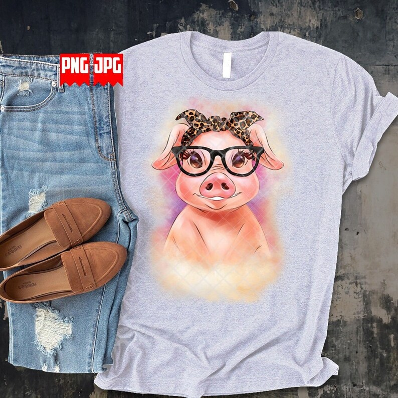 May include: A light gray t-shirt with a cartoon pig wearing glasses and a leopard print bandana. The pig is on a watercolor background with shades of purple, yellow, and orange.