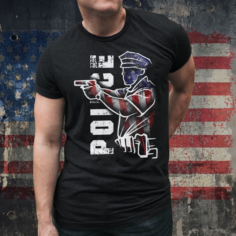 May include: Black t-shirt featuring a distressed graphic of a police officer aiming a handgun. The officer's silhouette is filled with the American flag design. The word "POLICE" is printed vertically in white, distressed font.