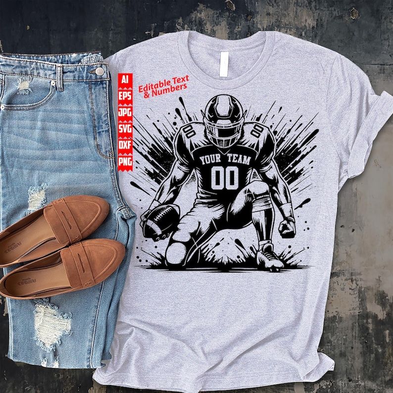 May include: A gray t-shirt featuring a black and white illustration of a football player in a kneeling position, holding a football. The text "YOUR TEAM" and the number "00" are visible on the jersey. The words "Editable Text & Numbers" are also present.