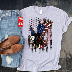 May include: A gray t-shirt with a distressed American flag design featuring a bald eagle with red, white, and blue feathers. The eagle is flying with its wings spread wide.