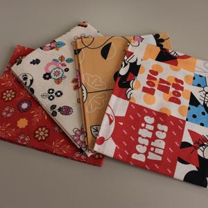 May include: Four patterned fabric napkins in a variety of colours. One is red with yellow flowers, another is cream with floral designs, a third is mustard yellow with black leaf outlines, and the last is white with red text that says "Love Dots" and "Bestie Vibes".