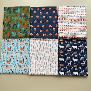 May include: Six fabric squares featuring various woodland-themed patterns. The designs include foxes, trees, mountains, and deer. The fabrics are in shades of blue, green, white, and orange.
