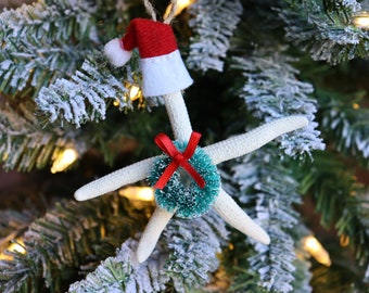 May include: A white starfish Christmas ornament with a green and white wreath and a red bow. The starfish is wearing a white and red Santa hat.