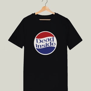 May include: Black t-shirt with a white circle graphic featuring the text "Dead inside" in blue and red lettering. The graphic resembles a soda can logo.
