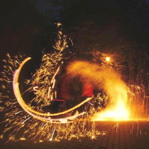 May include: Two people performing a fire show with glowing embers and sparks. The performers are wearing dark clothing and are holding metal objects that are spinning and creating fiery circles.