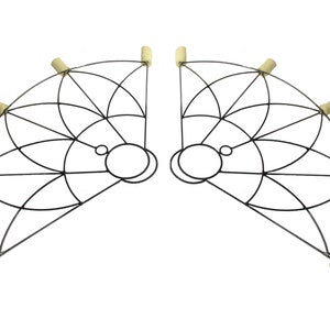 May include: A pair of black metal fire fans, each with a semi-circular frame and a geometric pattern. The fans have circular handles and beige wicks at the ends, designed for fire performance. The fans are symmetrical.