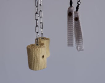 May include: Two fire poi with rolled wicks and silver chains, and two white fabric hand straps with rivets. The wicks are beige and the straps are white. The items are hanging against a light grey background.