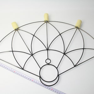 May include: A black metal fire fan with six yellow wicks. The fan has a geometric design and is measured with a tape measure. The fan is approximately 50 cm wide.