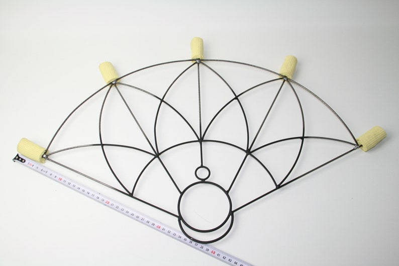 May include: A black metal fire fan with six yellow wicks. The fan has a geometric design and is measured with a tape measure. The fan is approximately 50 cm wide.