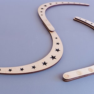 May include: Two wooden crescent moon shapes with black star cutouts. The moons are connected by a hinge and have small metal circles on the back.