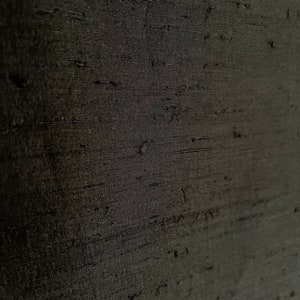 K&ouml;nnte beinhalten: Nahaufnahme eines schwarzen Stoffes mit einem strukturierten, gewebten Muster. Der Stoff hat einen dezenten Glanz und ein glattes, seidenweiches Gef&uuml;hl.
