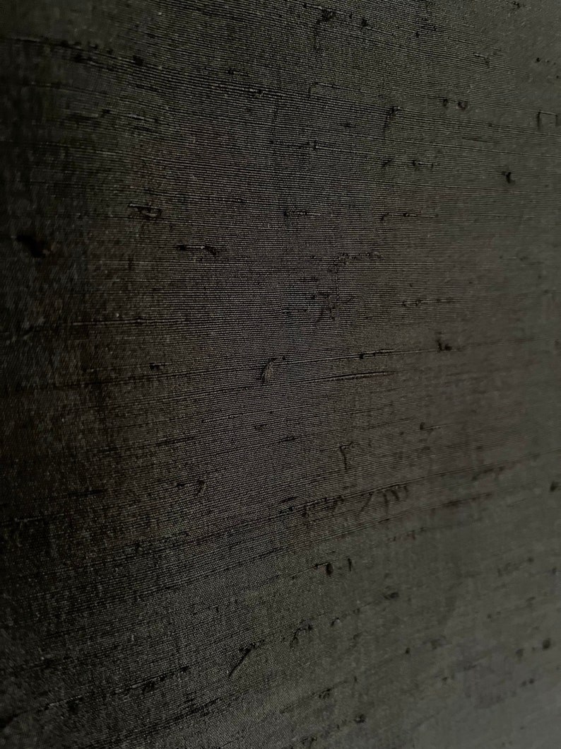 K&ouml;nnte beinhalten: Nahaufnahme eines schwarzen Stoffes mit einem strukturierten, gewebten Muster. Der Stoff hat einen dezenten Glanz und ein glattes, seidenweiches Gef&uuml;hl.