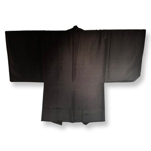 K&ouml;nnte beinhalten: Ein schwarzer Seiden-Haori, ein traditionelles japanisches Obergewand, mit schlichtem Design und glatter Textur.