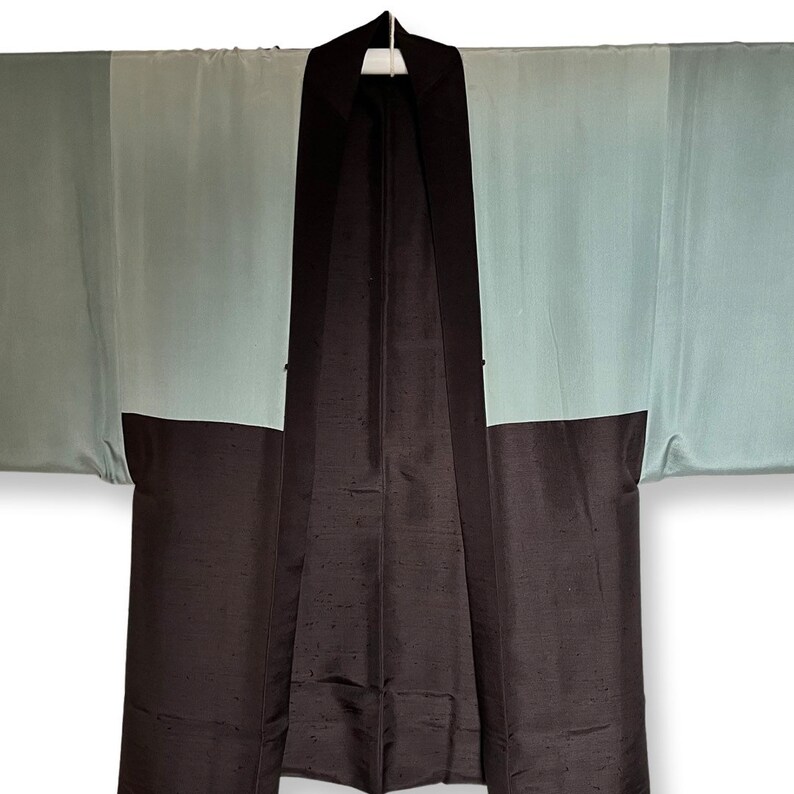 K&ouml;nnte beinhalten: Ein schwarzes und hellblaues japanisches Hanten, eine traditionelle kurze Jacke mit schlichtem Design. Die Jacke ist aus Seide und hat einen kragenlosen Ausschnitt.