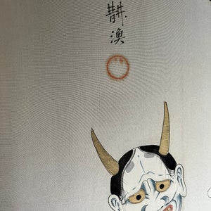 K&ouml;nnte beinhalten: Ein wei&szlig;er Hintergrund mit einer schwarz-wei&szlig;en japanischen D&auml;monenmaske mit goldenen H&ouml;rnern. Die Maske hat ein breites, zahniges Grinsen und gelbe Augen. Der Text "舞" und "楽" ist in schwarzer Tinte &uuml;ber der Maske geschrieben.