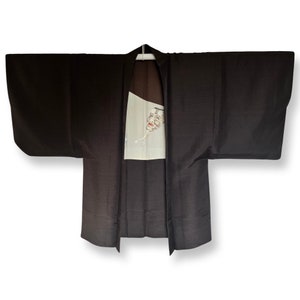 K&ouml;nnte beinhalten: Ein dunkelbraunes japanisches Hanten, eine traditionelle kurze Jacke, mit einem wei&szlig;en Panel, das ein gemaltes Design eines Gesichts zeigt.