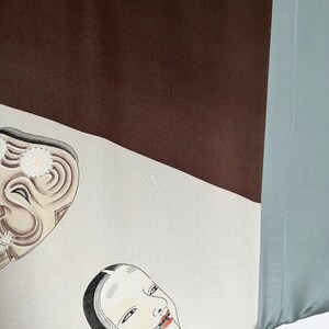 K&ouml;nnte beinhalten: Ein wei&szlig;er Stoff mit zwei schwarz-wei&szlig;en Masken. Die Masken sind auf den Stoff gemalt. Der Stoff ist Teil eines gr&ouml;&szlig;eren Stoffst&uuml;cks mit braunen und blauen Abschnitten.
