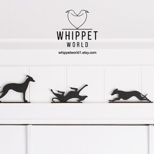May include: Black metal whippet dog silhouettes in various poses, displayed on a white surface. The silhouettes depict the dogs sitting, standing, rolling, running, and playing. The text "WHIPPET WORLD" and a website address are visible.