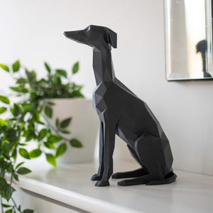 K&ouml;nnte beinhalten: Eine schwarze, geometrische Hundeskulptur mit langem Hals und spitzen Ohren steht auf einem wei&szlig;en Regal. Das moderne Kunstwerk befindet sich neben einem wei&szlig;en Pflanzgef&auml;&szlig; mit gr&uuml;nen Bl&auml;ttern und einem Spiegel.