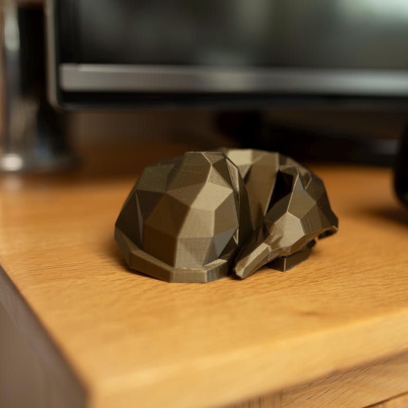 K&ouml;nnte beinhalten: Eine geometrische, polygonale Skulptur eines schlafenden Fuchses in Braun- und Graut&ouml;nen. Die Fuchsskulptur liegt auf einer Holzoberfl&auml;che mit verschwommenem Hintergrund. Die Skulptur hat ein modernes, minimalistisches Design.