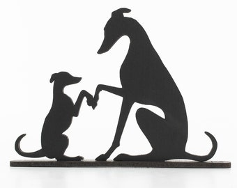 Op de afbeelding: Zwarte silhouet van twee whippet-honden, een zittend en de andere staand op zijn achterpoten, met hun poten die elkaar raken. De honden staan op een bruine houten basis. De tekst "Whippet World" staat boven de honden.