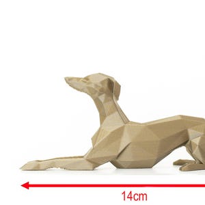 K&ouml;nnte beinhalten: Eine geometrische, hellbraune Hundeskulptur in liegender Pose. Die Skulptur ist 14 cm lang und 6,5 cm hoch. Die Form des Hundes besteht aus mehreren flachen Ebenen, was ihr ein modernes, eckiges Aussehen verleiht. Auf wei&szlig;em Hintergrund.