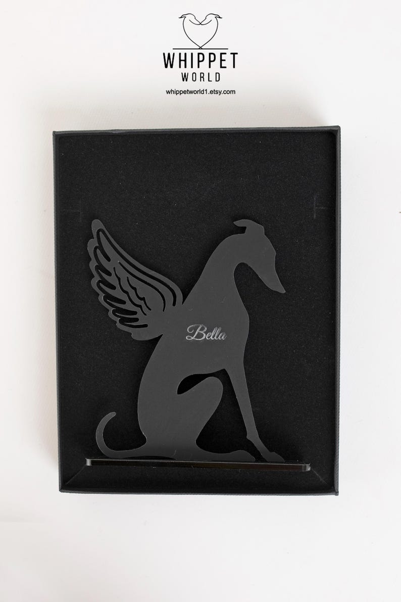 Op de afbeelding: Zwart metalen silhouet van een hond met engelen vleugels, gepersonaliseerd met de naam "Bella". Het kunstwerk wordt gepresenteerd in een zwarte doos, met het "Whippet World" logo en website adres bovenaan.