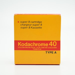 Puede incluir: Una caja amarilla con texto rojo para un cartucho de película super 8 Kodakchrome 40. El texto en la caja dice "super 8 cartridge, chargeur super 8, super 8 Kassette, Kodachrome 40, Colour Movie Film, Film Cine en Couleurs, Farbfilm, Type A".