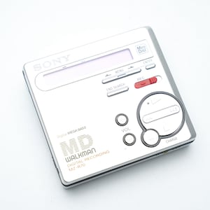 Könnte beinhalten: Silberner Sony Walkman MZ-R70 MiniDisc-Player. Er verfügt über einen Bildschirm, Steuertasten und einen Lautstärkeregler. Das Gerät trägt die Aufschrift "Digital Mega Bass" und "Walkman Digital Recording MZ-R70".