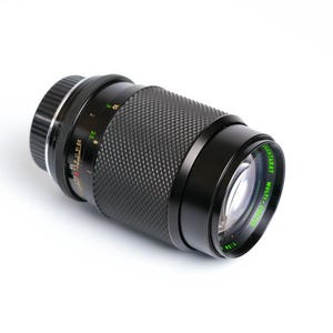 May include: A black camera lens with a green "Multi-Coated Multi-Ray" label. The lens has a textured surface and a silver ring around the front.