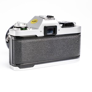 May include: Silver and black vintage camera with a textured grip. The camera has a lens, viewfinder, and a yellow "PASSED" sticker. The camera strap is black. The camera is on a white background.