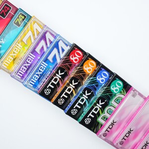 May include: A stack of vintage audio cassette tapes in various colors and brands, including Sony, Maxell, and TDK. The tapes are labeled with different lengths, including 74 and 80 minutes.