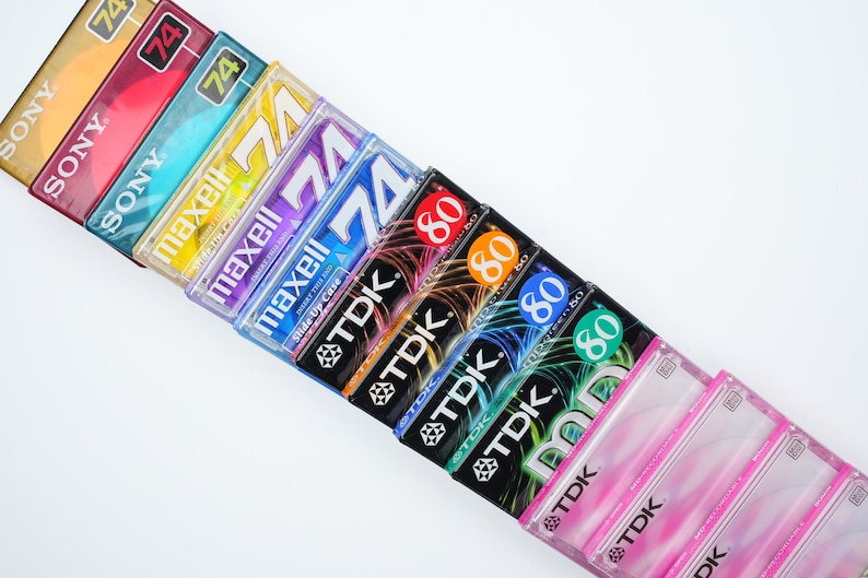 May include: A stack of vintage audio cassette tapes in various colors and brands, including Sony, Maxell, and TDK. The tapes are labeled with different lengths, including 74 and 80 minutes.