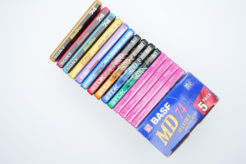 May include: A stack of various brand mini disc audio recording media, including Sony, TDK, and BASF. The top disc is a blue and white BASF MD 74 Maxima Digital Audio 5 pack.