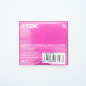 May include: Pink TDK Mini Disc packaging with the text "Mini Disc, Recordable, Rewritable, Mini Disc, Enregistrable, Mini Disc, Rewritable, Mini Disc, gravabile, Mini Disc, riscrivibile, Mini Disc, nagrywalne, Mini Disc, regrav&aacute;vel, Mini Disc, grav&aacute;vel, Mini Disc, перезаписываемый, Mini Disc, записываемый, Mini Disc, قابل إعادة الكتابة, Mini Disc, قابل للتسجيل, TDK POLSKA Sp. z o.o. 71-713 Szczecin ul. Dąbrowskiego 1A, POLAND" and a barcode with the item code "MO-C80PELC".